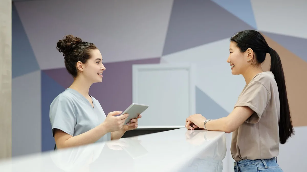 A receptionist with a tablet greeting a visitor at a front desk