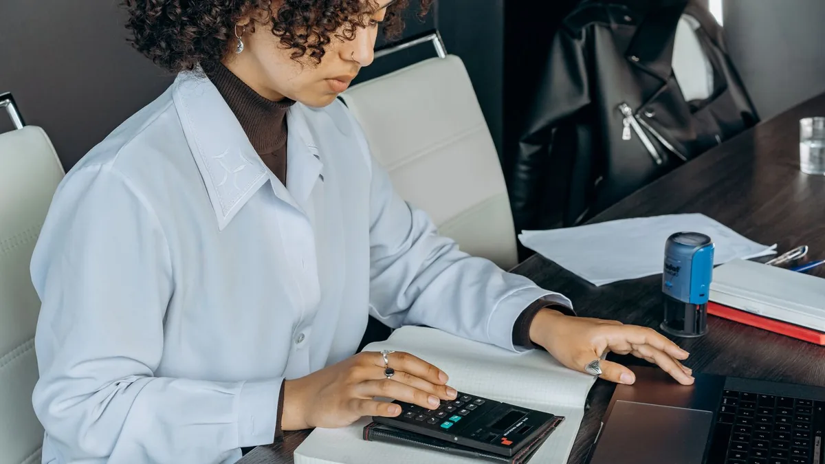 A bookkeeper working at a laptop alongside a desktop calculator and ledgers